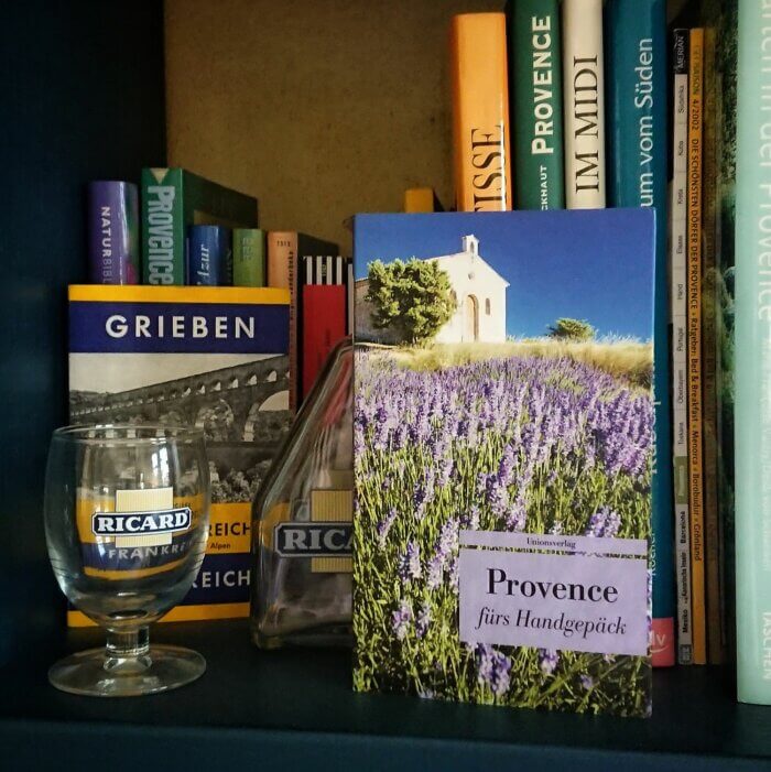 Provence fürs Handgepäck. Das Taschenbuch steht in einem Buchregal voller Bücher über die Provence, daneben ein Pastis Glas