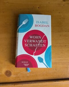 Isabel Bogdan. Wohnverwandschaften. Der Roman liegt auf einer Holzoberfläche.