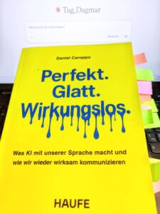 Das Buch "Perfekt, glatt, wirkungslos: Was KI mit unserer Sprache macht und wie wir wieder wirksam kommunizieren" von Daniel Caroppo liegt auf einer Computertastatur. Auf dem Bildschirm im Hintergrund sieht man leicht verschwommen ein offenes Chatfenster der KI Claude.